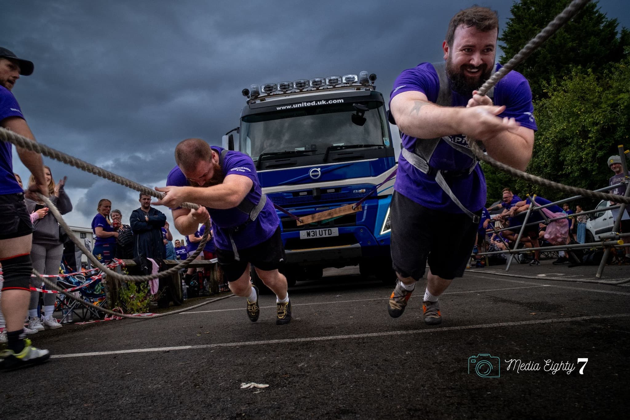 Two strongmen pulling a Volvo United truck across a wet car park